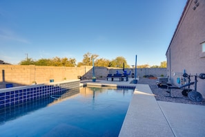 Una piscina con piastrelle blu, una zona patio con mobili da esterno e attrezzature per esercizi.