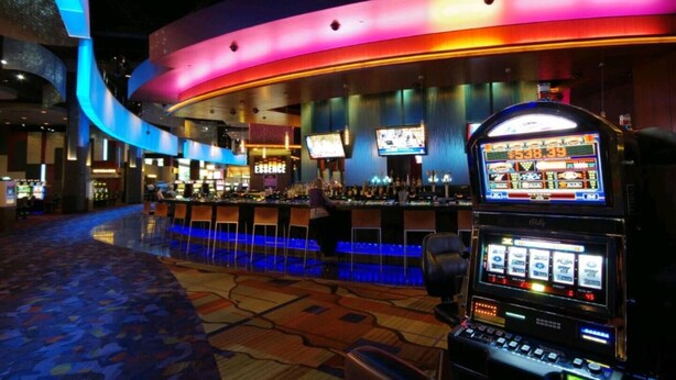 Interior de un casino con máquinas tragamonedas, una zona de bar y una pared curva con iluminación de neón.