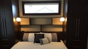 Una habitación de hotel con una cama grande, dos lámparas de noche, un televisor sobre la cama y muebles de madera oscura.