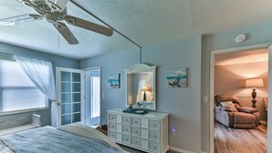 Une chambre à coucher comprenant un lit, une commode, un ventilateur de plafond et une porte donnant sur une autre pièce.