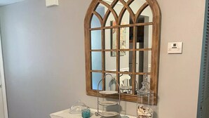 Une console blanche, dotée d’une vitrine et agrémentée d’objets décoratifs, est placée devant un mur sur lequel est accroché un grand miroir en arc de cercle.