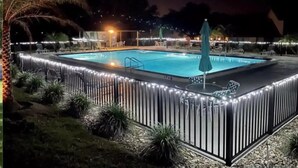 Une piscine rectangulaire dotée d’une terrasse carrelée, entourée d’une clôture agrémentée de guirlandes lumineuses.