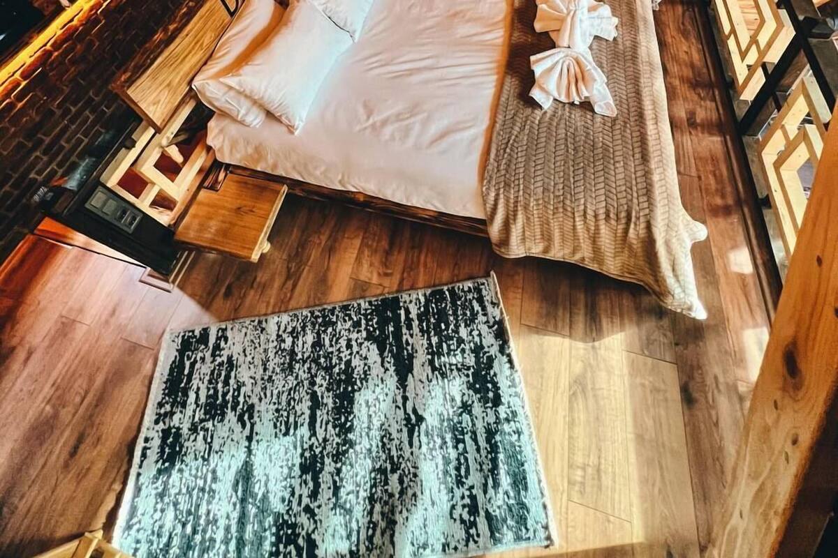 Een houten kamer met een bed, een klein tafeltje en een vloerkleed.