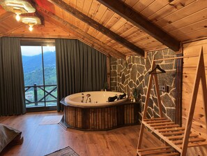 Une cabane en bois avec un mur en pierre, une grande baignoire et un balcon offrant une vue sur les montagnes.