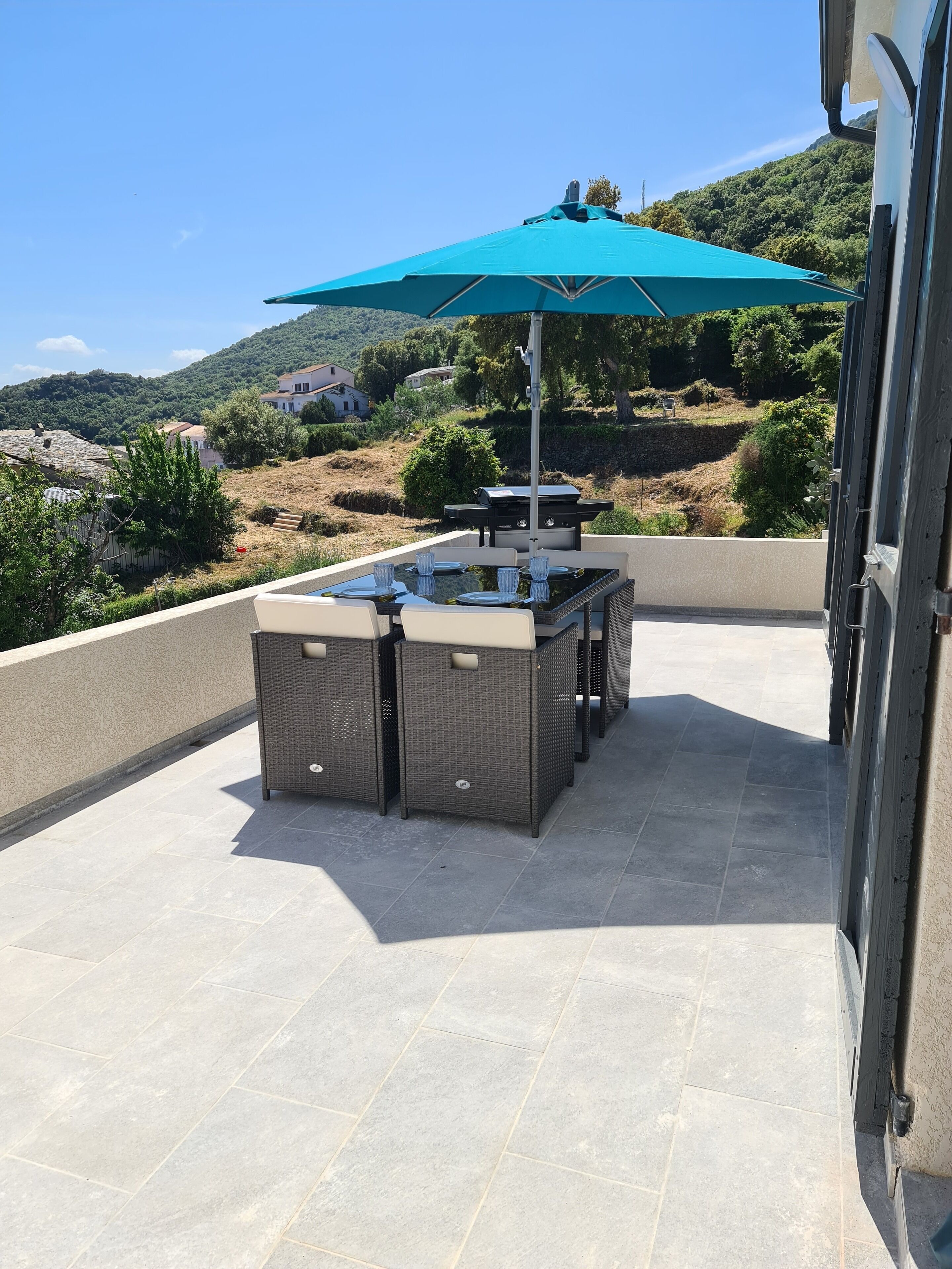 An outdoor patio with a dining table and chairs, a grill, and a large umbrella.