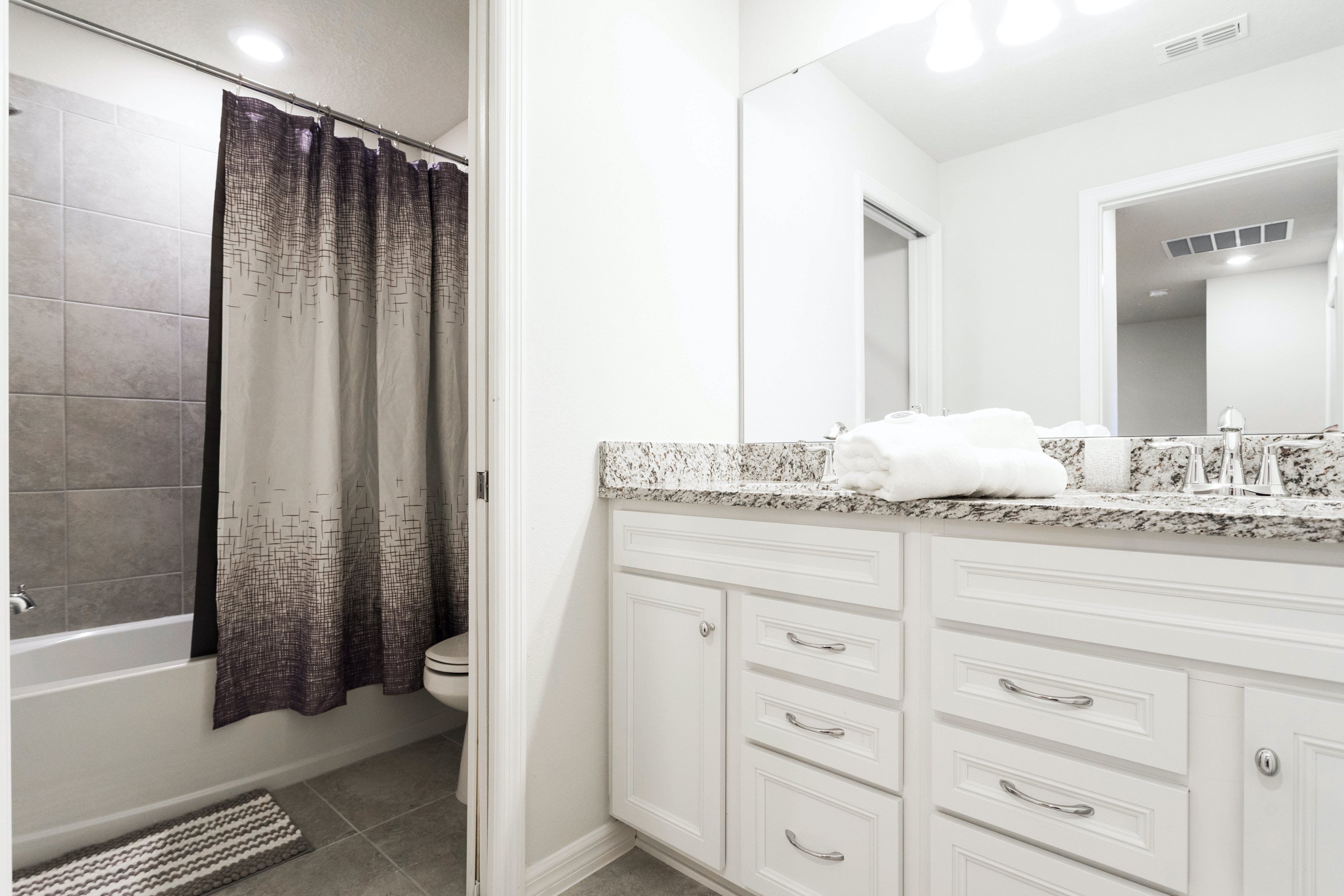 A bathroom with a bathtub, a shower curtain, a toilet, and a vanity with drawers and a mirror.