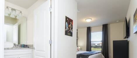 Una camera da letto con un letto, una cassettiera, uno specchio, una TV e una finestra con tende.