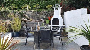 Un patio al aire libre con suelo de piedra, mobiliario de mimbre y un horno exterior blanco.