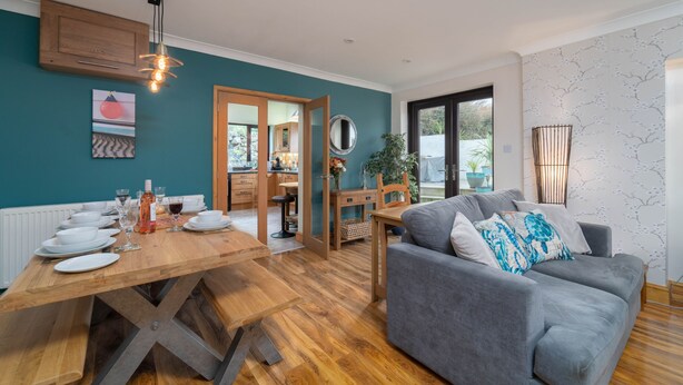 Una sala de estar moderna con un sofá gris, una mesa de comedor de madera y paredes color esmeralda.