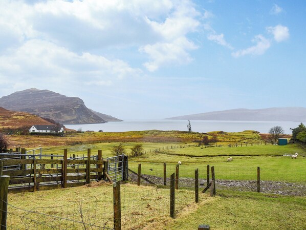 A rural landscape with a house, a fenced field, and a body of water in the distance.