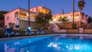 Una casa de dos pisos con piscina, mobiliario exterior y una escalera que lleva a un balcón.