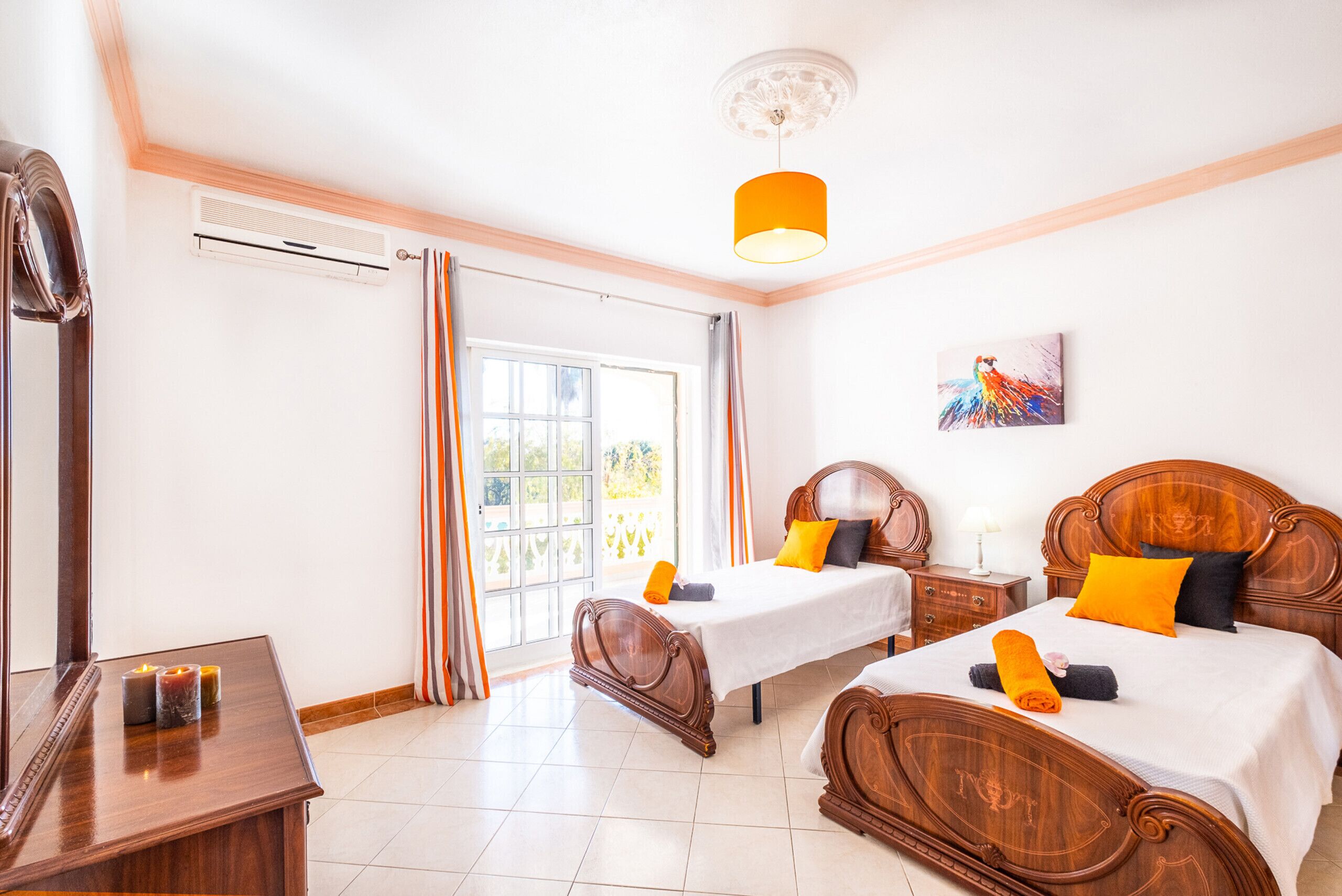 A hotel room with two wooden beds, a large window with curtains, a ceiling fan, and a painting on the wall.