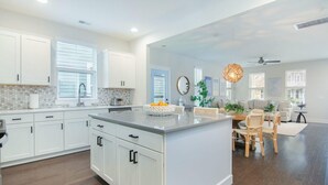 A spacious kitchen with white cabinetry, a large island, and a dining area with wooden chairs. - Happy Ours, Mins to Park Circle, Dtwn, CHS Beach (North Charleston)