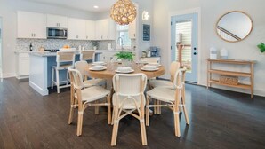 A modern kitchen with white cabinets, a central island, and a dining area with wicker chairs. - Happy Ours, Mins to Park Circle, Dtwn, CHS Beach (North Charleston)