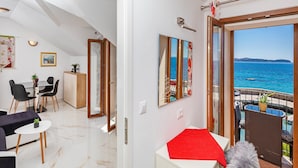 Un salon moderne avec un coin repas, un grand miroir qui reflète la vue sur la mer et un balcon donnant sur l’océan.