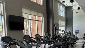 Un gimnasio con varias cintas de correr alineadas frente a una pared con ventanas.