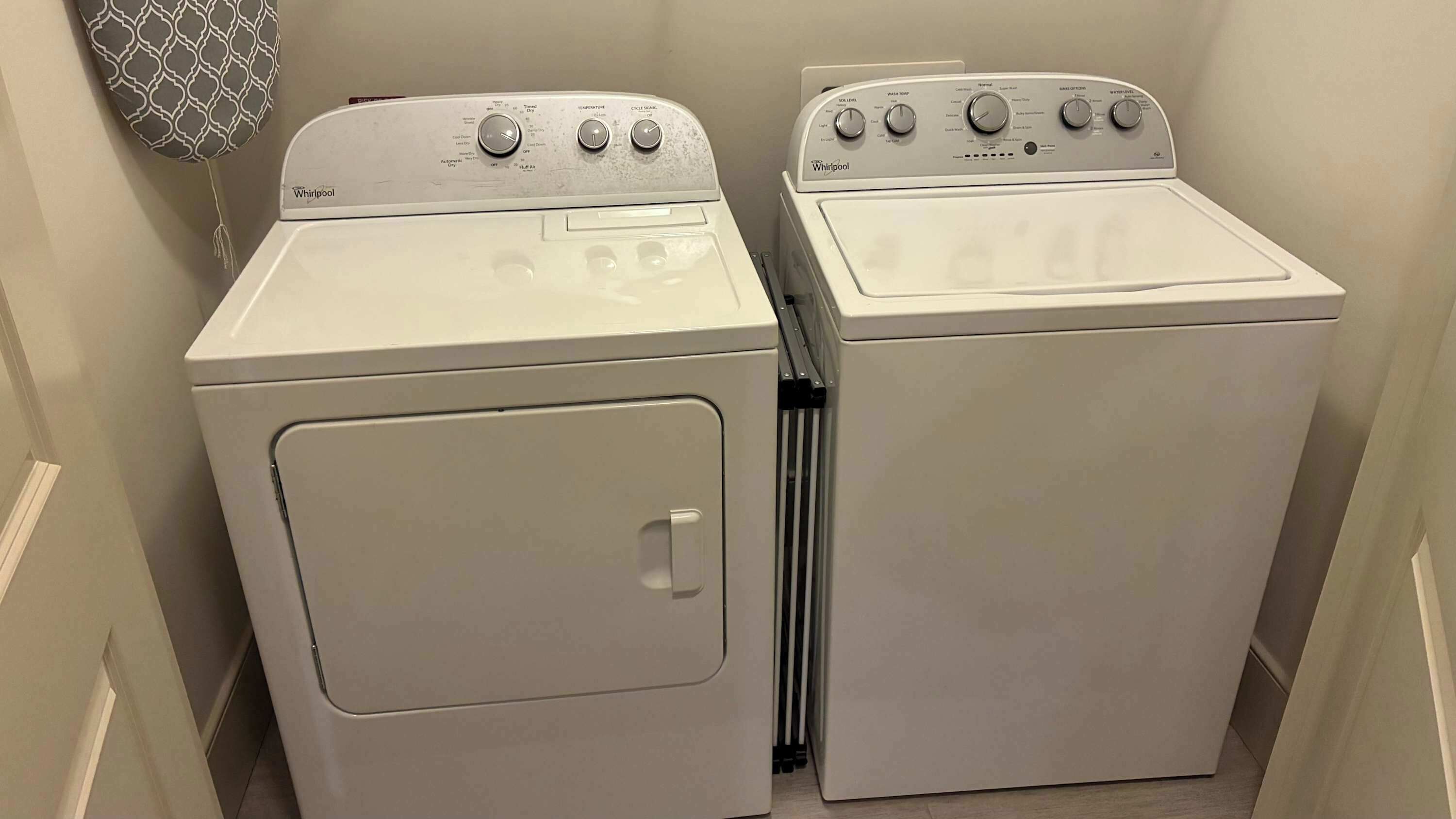 Deux machines à laver Whirlpool blanches se trouvent dans une buanderie, avec une décoration murale à motifs.