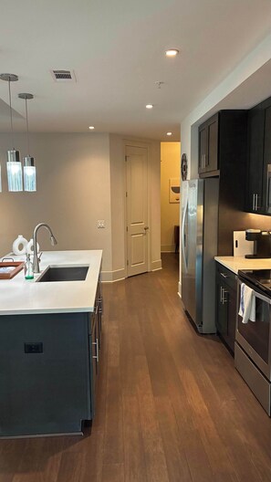 A modern kitchen with a central island, stainless steel appliances, and a wooden floor.