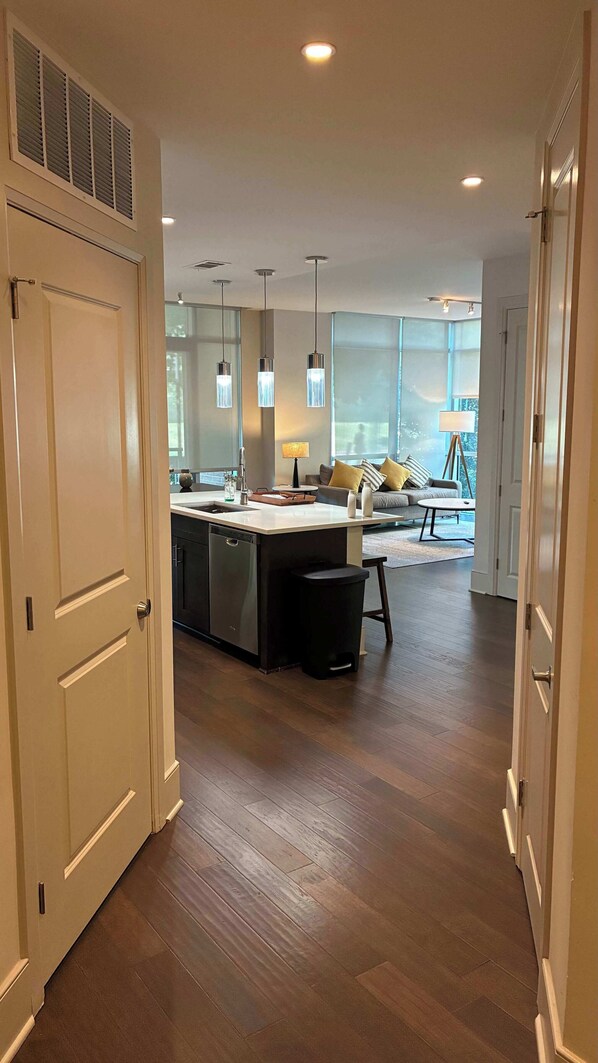 A modern kitchen with a central island, a dining area with a sofa and table, and a view through large windows.