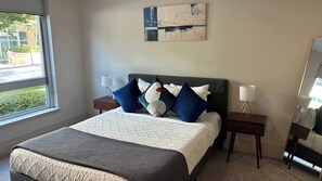 Una habitación de hotel con una cama, dos mesitas de noche, una ventana y un cuadro en la pared.
