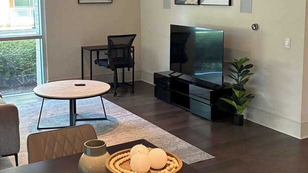 Un salon moderne doté d’un téléviseur à écran plat, d’une table à manger agrémentée d’objets décoratifs et d’une grande fenêtre laissant entrer la lumière naturelle.