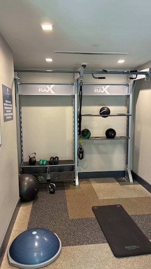 Un gimnasio con barra de dominadas, kettelbells, balón medicinal y colchoneta.