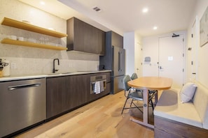 Una cocina moderna con electrodomésticos integrados, estantes de madera y un comedor con mesa y sillas.