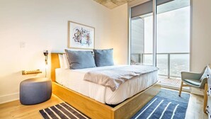 Een moderne slaapkamer met een groot bed, een nachtkastje, een stoel, een raam met uitzicht en een kunstwerk aan de muur.