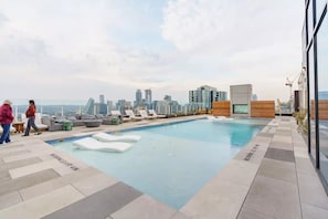 Piscina en la azotea con sillones de descanso y vista al horizonte urbano.