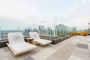 Une terrasse sur le toit, avec des chaises longues, une petite table et un jardinier avec des plantes.