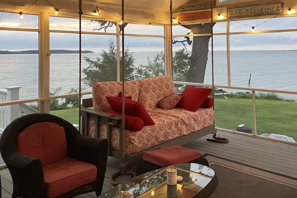 Swinging daybed, cushioned outdoor furniture set on screen porch.
