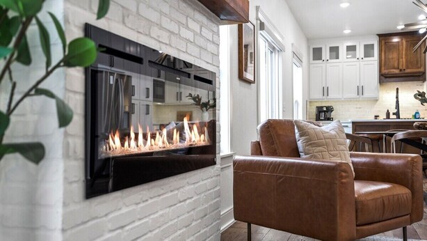 A modern living room with a fireplace, leather sofa, and a kitchen area in the background.