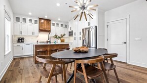 A modern kitchen with white cabinets, a central island, and a dining area with wooden chairs.