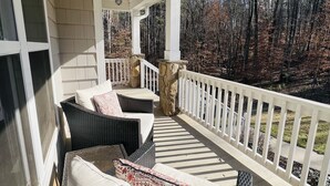 A covered porch with wicker furniture, a stone pillar, and a view of a wooded area. - Spacious Lake Norman Waterfront with hot tub, game room, kayaks & SUPs! (Mooresville)