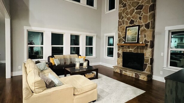 A spacious living room with a high ceiling, a stone fireplace, and a large window. - Spacious Lake Norman Waterfront with hot tub, game room, kayaks & SUPs! (Mooresville)