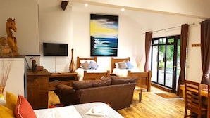 A cozy room with a large window, a flat-screen TV, a wooden bed, a brown leather sofa, and a wooden desk with a vase and a bird figurine.