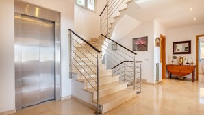 A modern interior with a spiral staircase, a stainless steel elevator, and a wooden table with decorative items. - VILLA BENDINAT 10 - by Priority Villas (Bendinat)