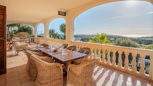 A terrace with a dining table and wicker chairs, overlooking a scenic landscape. - VILLA BENDINAT 10 - by Priority Villas (Bendinat)