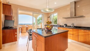 A modern kitchen with a central island, wooden cabinets, and a view of the outdoors. - VILLA BENDINAT 10 - by Priority Villas (Bendinat)