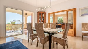 A dining area with a glass table, wicker chairs, and a view of the outdoors. - VILLA BENDINAT 10 - by Priority Villas (Bendinat)