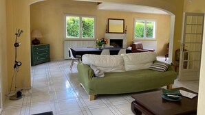 A living room with a green sofa, a dining table, and a fireplace. - Villa * Coulommiers * Parcs des félins * Provins * Gîte de la moinerie (Beautheil-Saints)