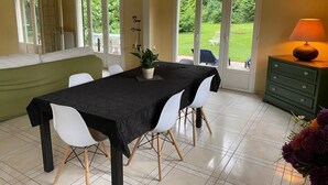 A dining area with a table set for four, white chairs, a green sofa, and a view of a garden through large sliding doors. - Villa * Coulommiers * Parcs des félins * Provins * Gîte de la moinerie (Beautheil-Saints)