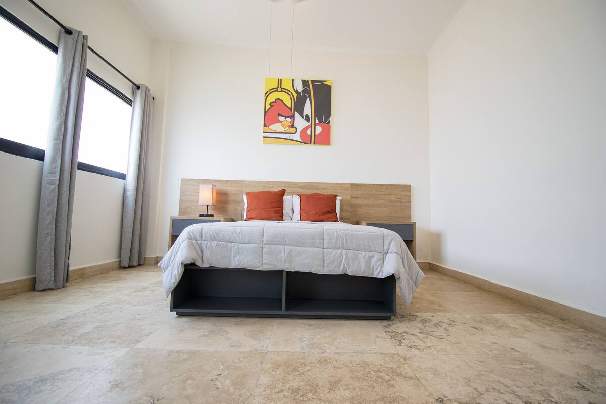 A modern bedroom with a bed, curtains, a headboard, and a wall art piece.