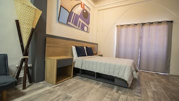 Een slaapkamer met een bed, een houten nachtkastje, een bureau, een stoel en een groot raam met gordijnen.