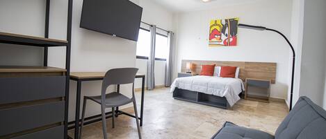 Quarto moderno com cama, escrivaninha, cadeira e televisão na parede.