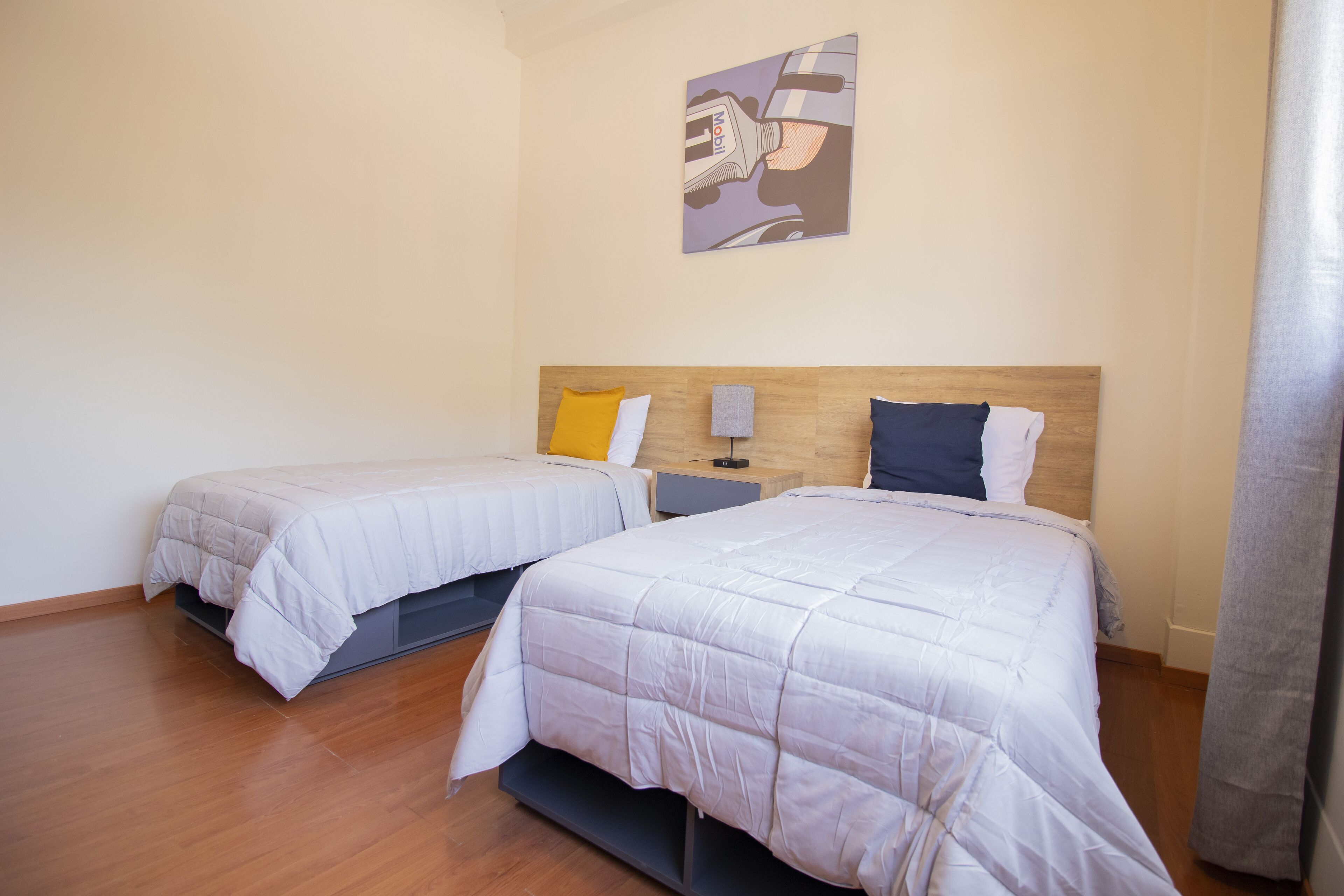 Two single beds with wooden headboards, a small bedside table, and a wall-mounted artwork.
