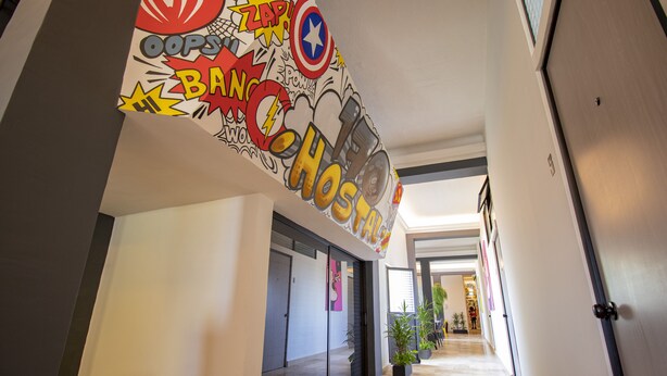 Um corredor com um mural vibrante em estilo de história em quadrinhos na parede, uma porta com puxador e um vaso de planta.