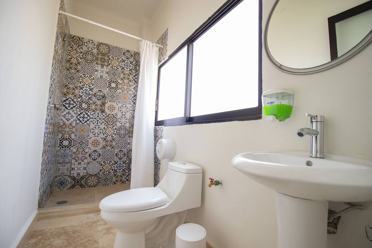 A bathroom with a patterned shower wall, a toilet, a sink, and a window.