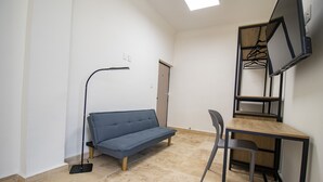 Quarto com sofá, escrivaninha com cadeira, televisão e vassoura.