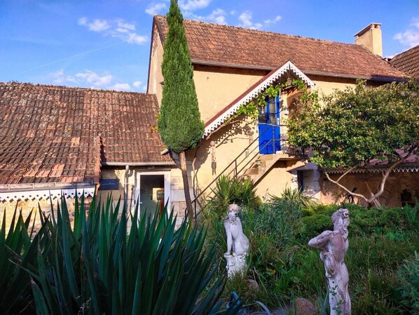 A traditional building with a tiled roof, a staircase with blue shutters, and statues in the foreground.